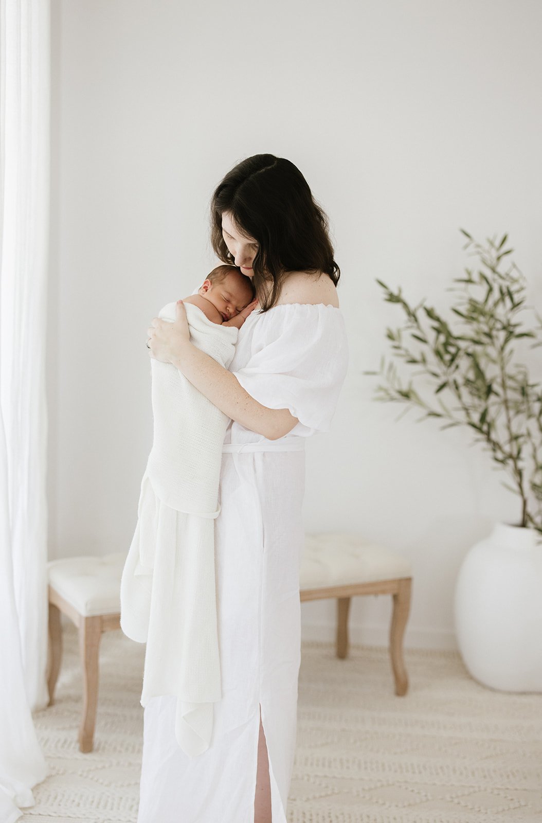  new mum cuddling her newborn baby both dressed in white 