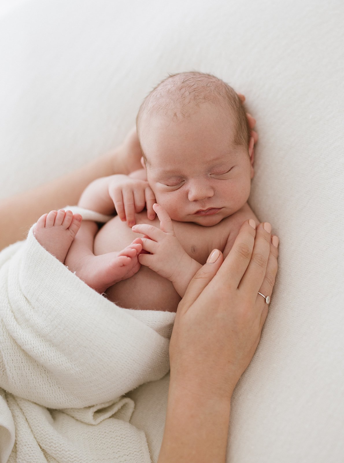  newborn baby cuddled up in the hand of its mum  