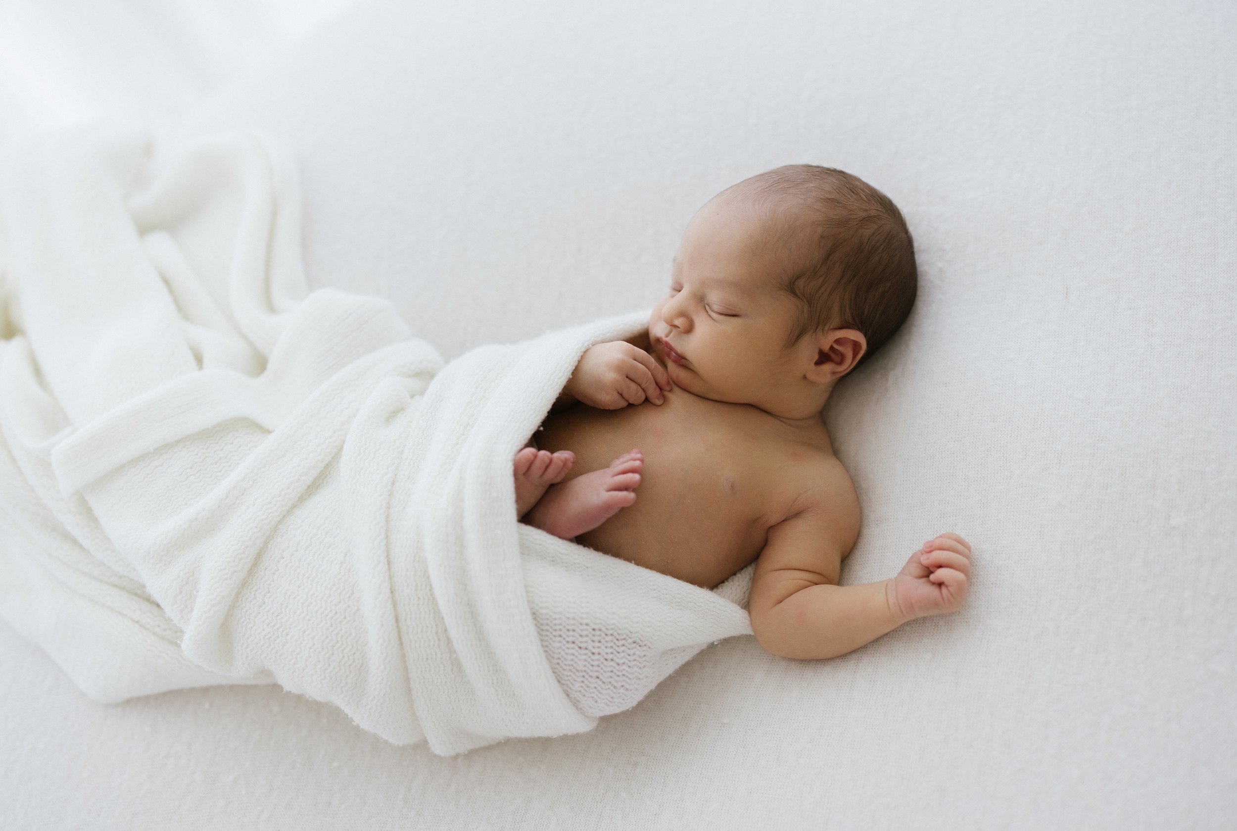  newborn baby cuddled up in a white wrap blanket  