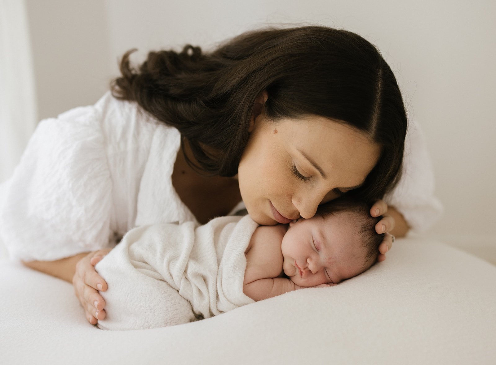 Newborn baby on white blanket being cuddled by her mum with long dark hair