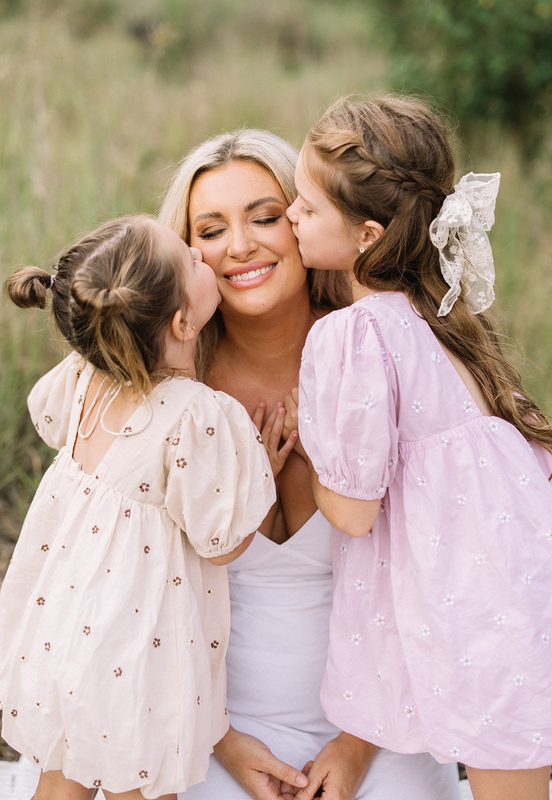 A mother is surrounded by her two daughters as they give her a kiss on each cheek 