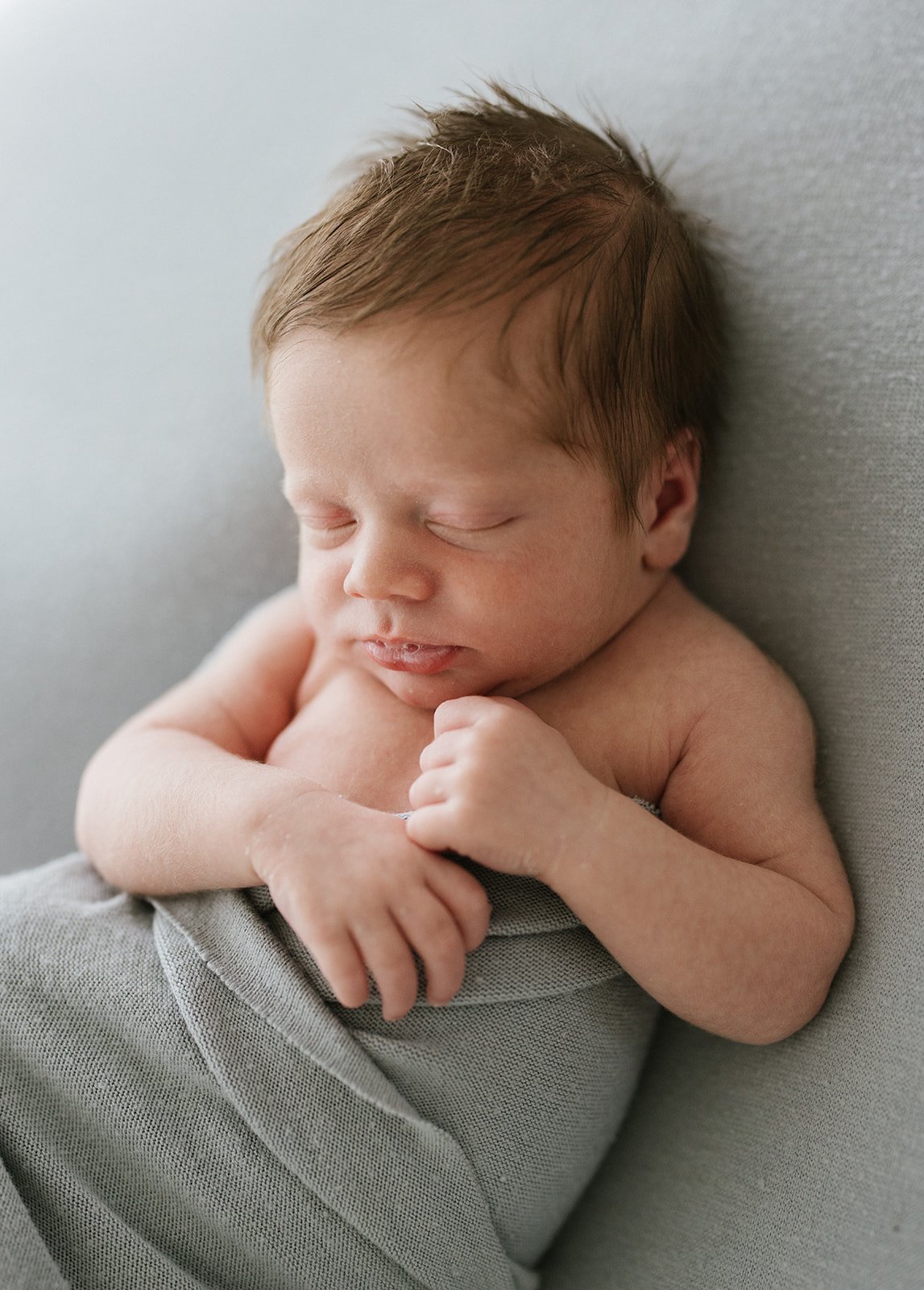 Photographed is a baby wrapped in a blue blanket. They have thick brown hair