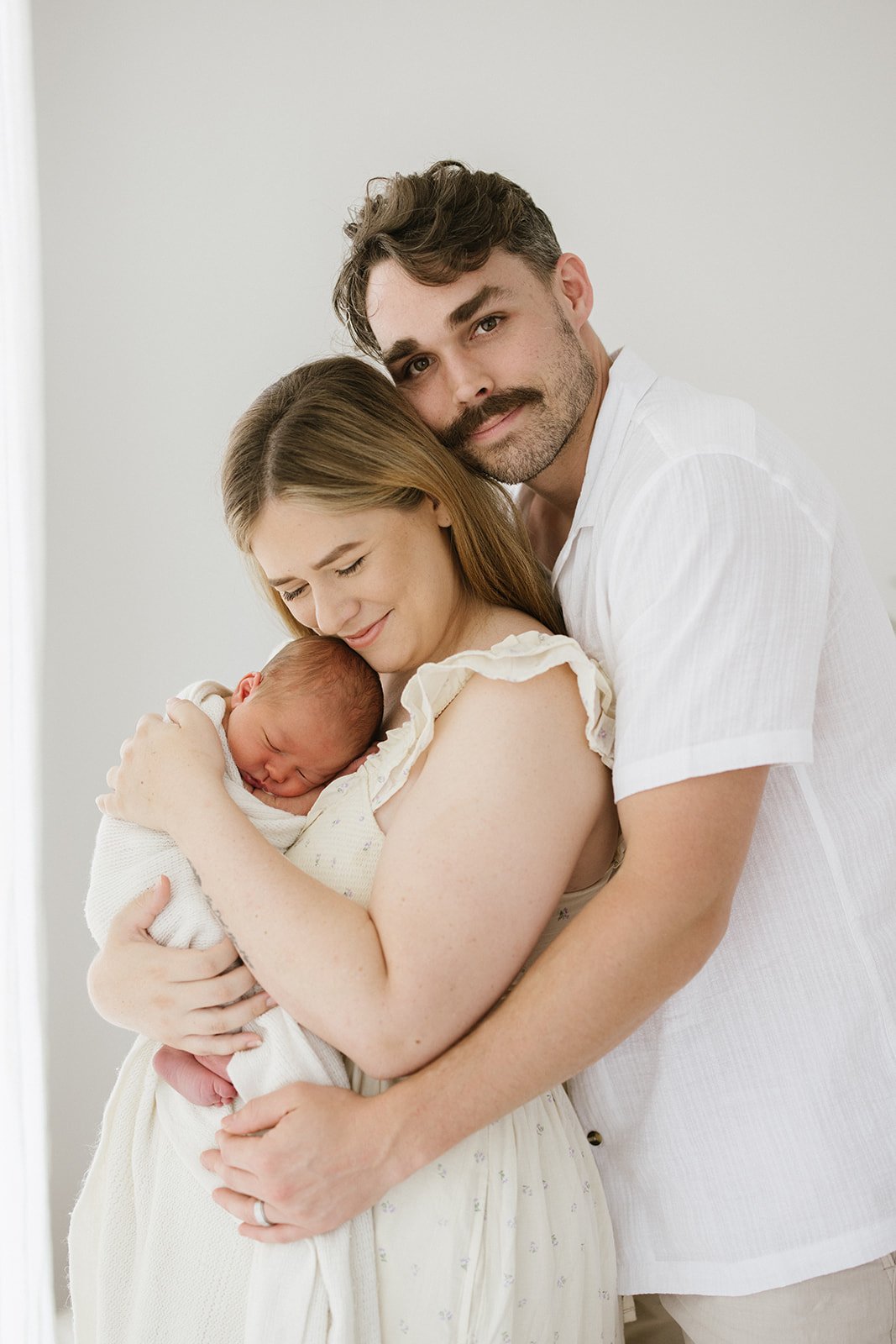  A dad cuddles into his wife who is holding their newborn baby.  