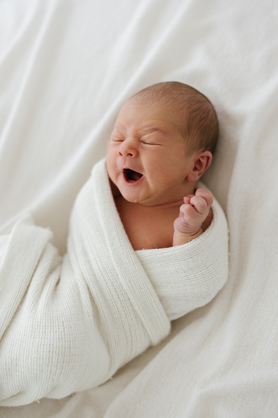 A photographer of a baby having a big yawn as they are laying on a white blanket