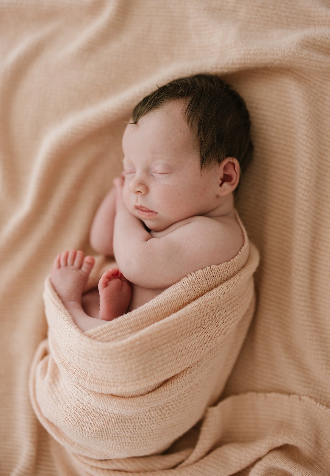 a newborn baby girl wrapped loosely in a pink blanket is all curled up during their newborn photoshoot