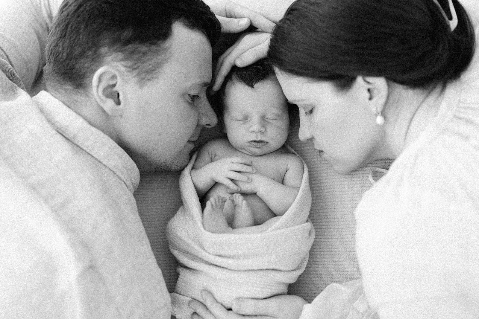 A mother and father cuddle right into their newborn daughter. The photograph is black and white