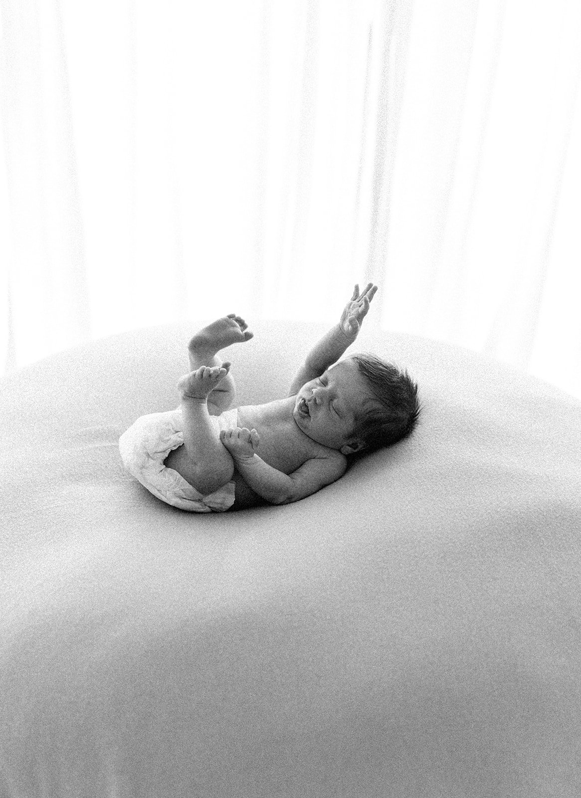 a black and white photo of a newborn baby wearing a just a nappy while it gives a big post nap stretch