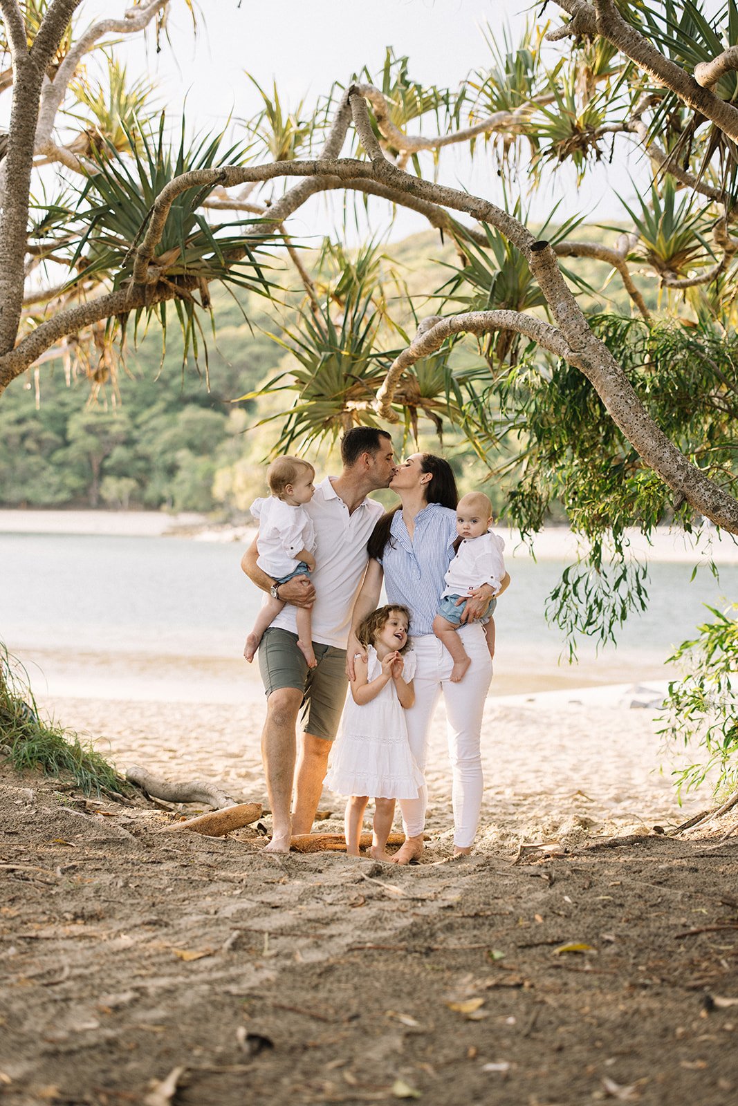 a family session held at Gold Coast Tallebudgera creek. The family are in blue and white outfits underneath palm trees by the ocean