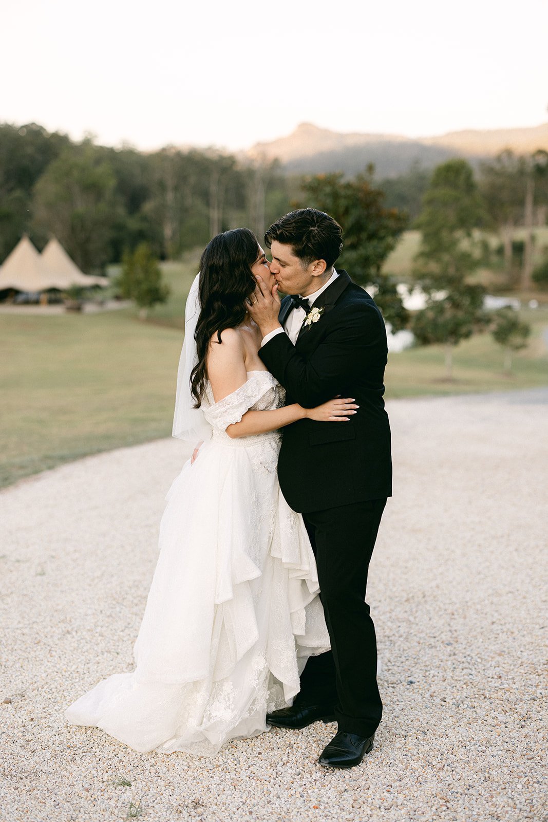 A bride and groom share a kiss on a white pebbled path at Gold Coast Farmhouse