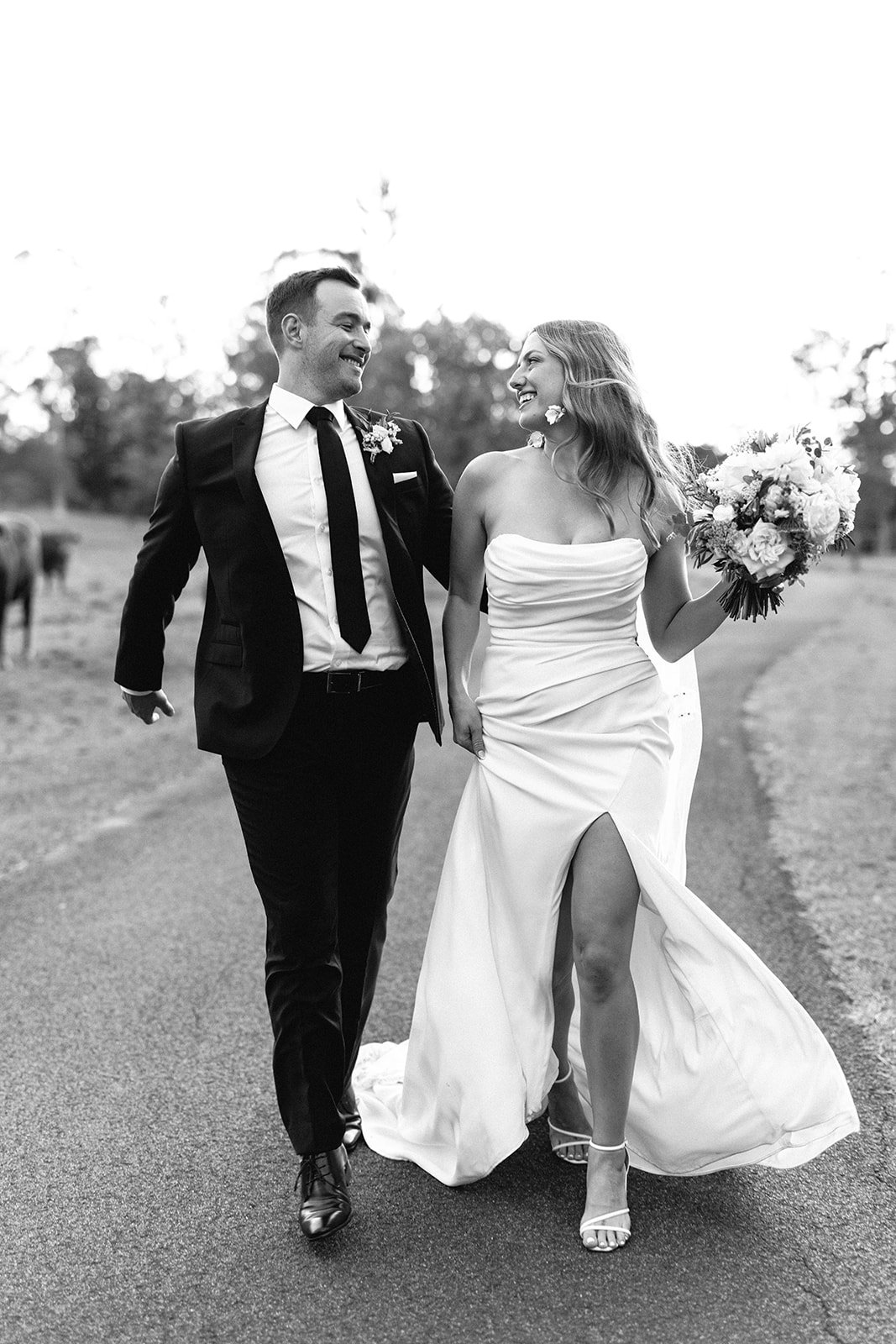 A black and white photograph of a couple who have just been married walking and laughing together