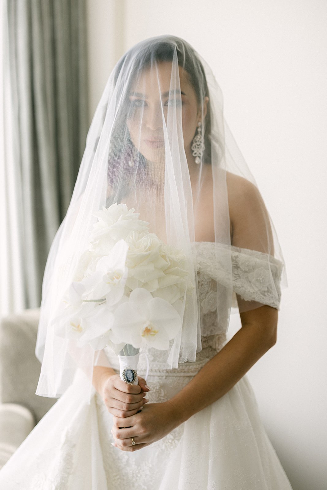 A bride with long dark hair is covered in a white wedding veil 