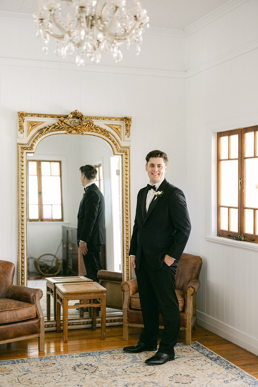 A groomsman is getting ready for his wedding standing in front of a large gold framed mirror 