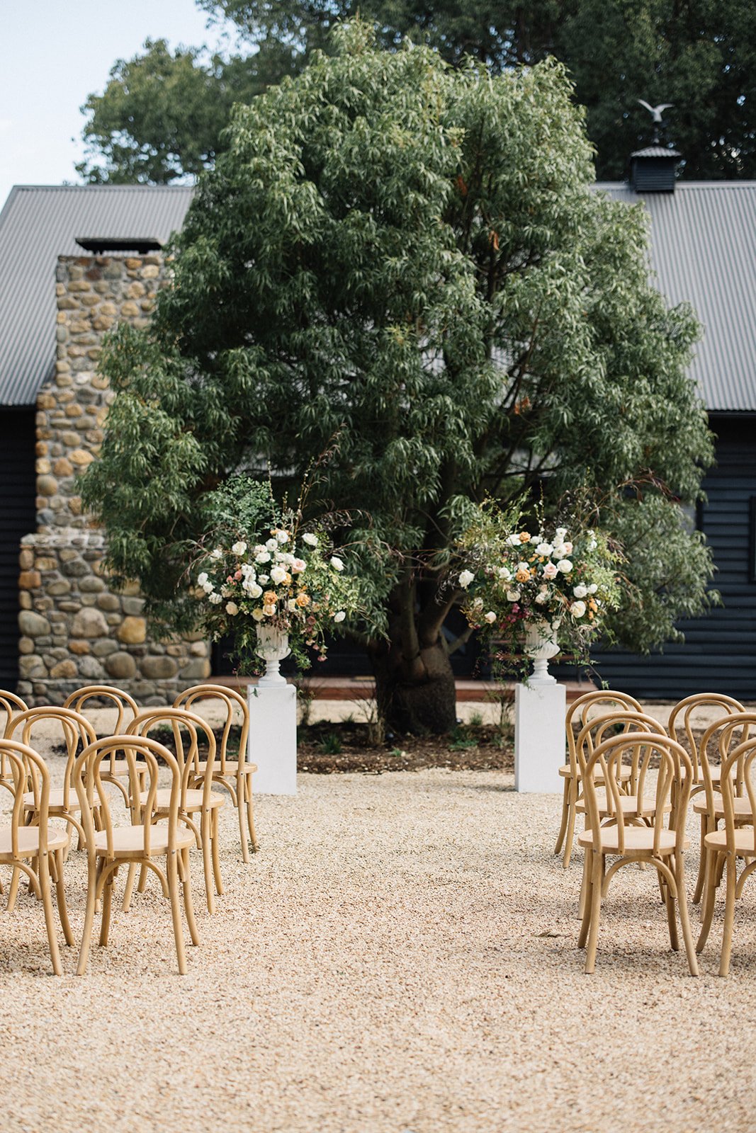 Kwila Lodge ceremony venue set up with bentwood chairs, two floral plinths and a large fig tree