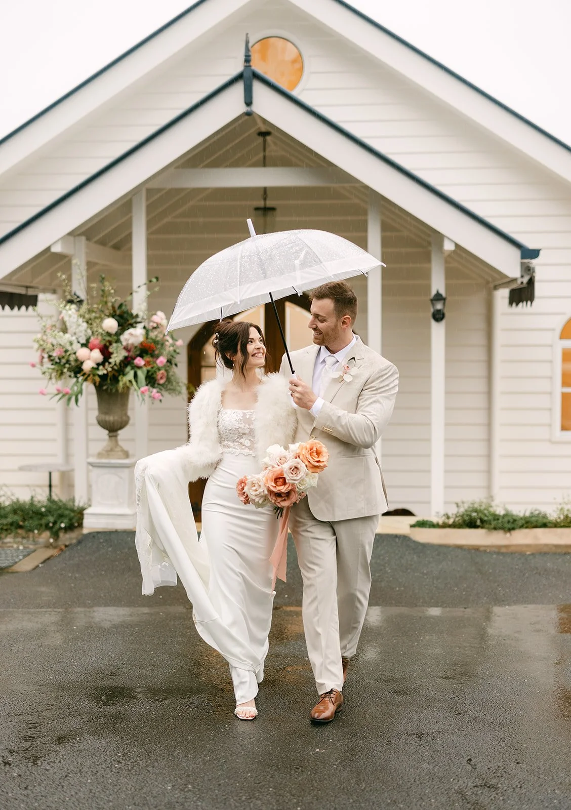 Groom holding umbrella over bride as they walk out of ceremony venue.