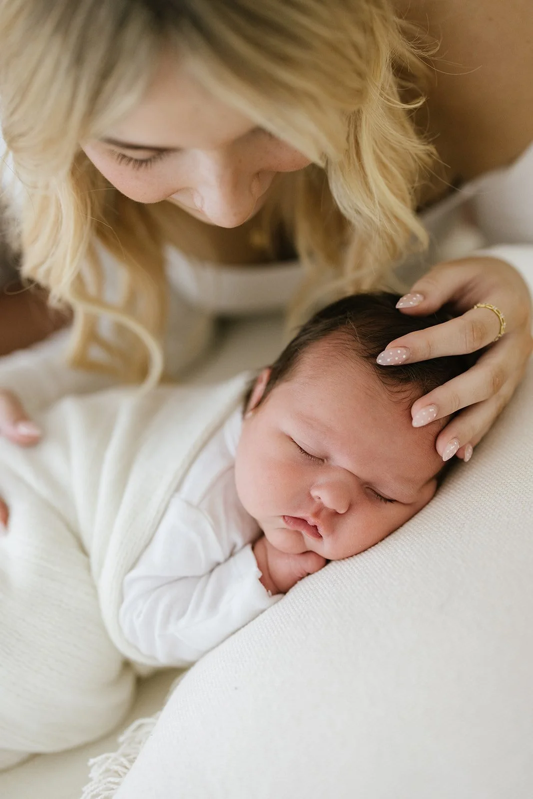 A mother gently cradles her sleeping baby, touching the baby's head with her hand while looking down affectionately. Taken at Wylde Folk Studio - Brisbane newborn photography.