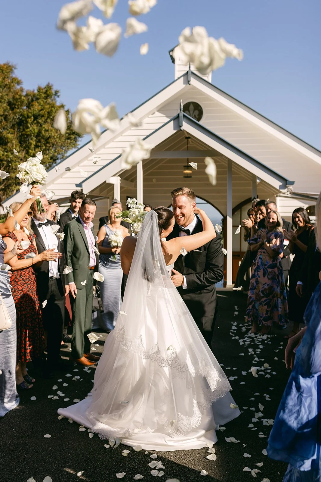 Bride and groom in-front of venue with petals flying in the air and family watching