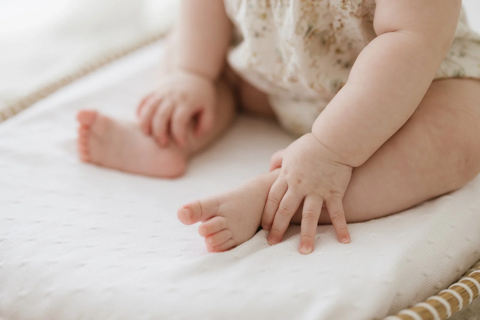 A close-up of a baby's hand touching their foot on a white surface. Taken at Wylde Folk Studio - Brisbane newborn photographer.