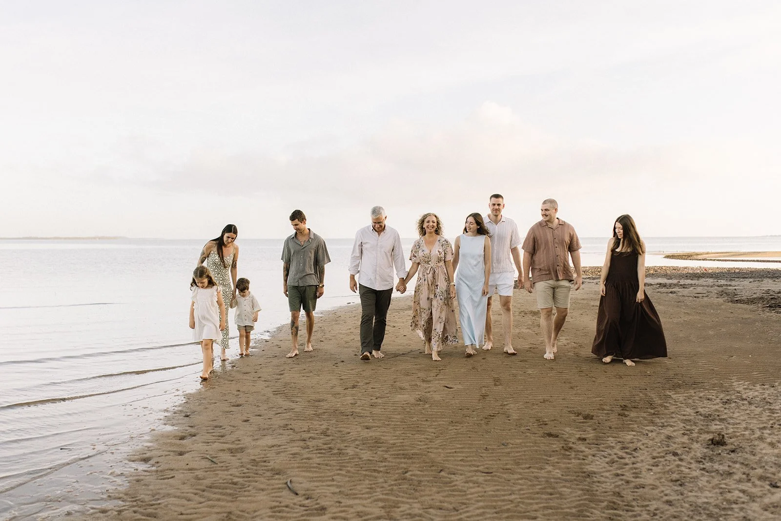 A multi-generational family walking on the beach near the shoreline, holding hands and enjoying a peaceful moment together. Taken by Wylde Folk Studio, Brisbane. Family photography.