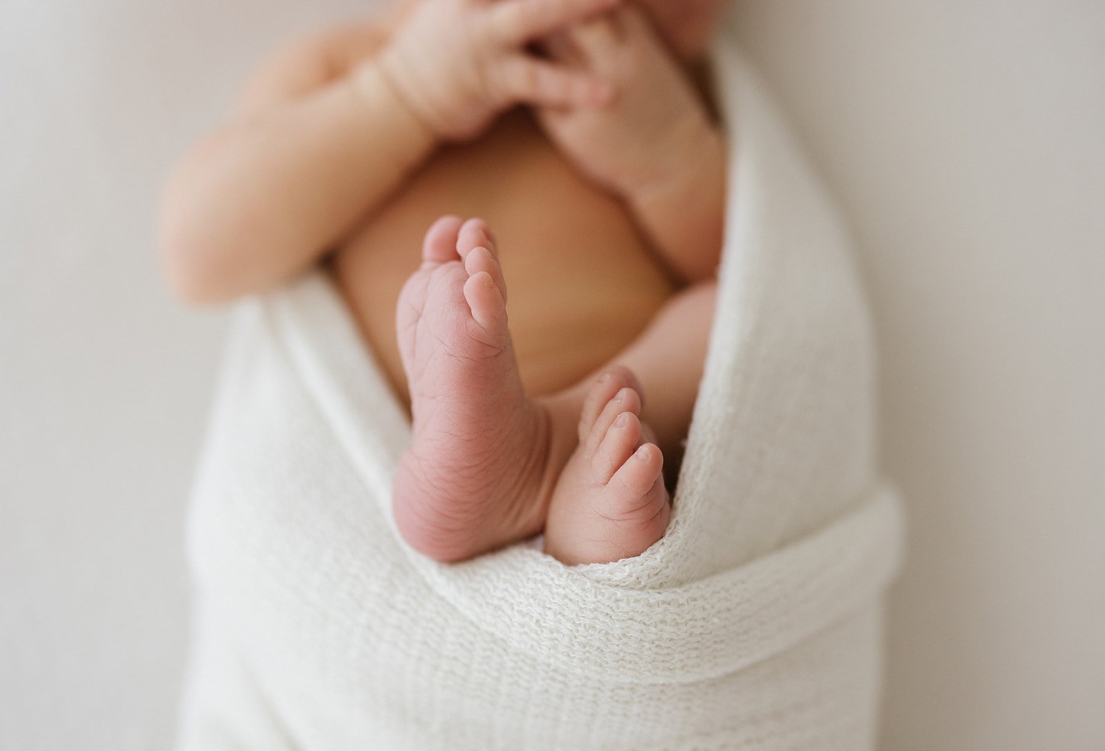 Close-up photograph of newborn baby's feet swaddled in white blanket