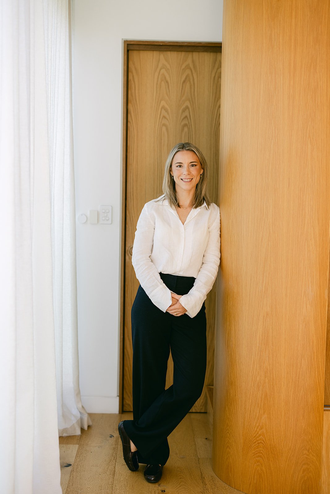 A woman wearing professional clothing is leaning on a wooden wall for a headshot