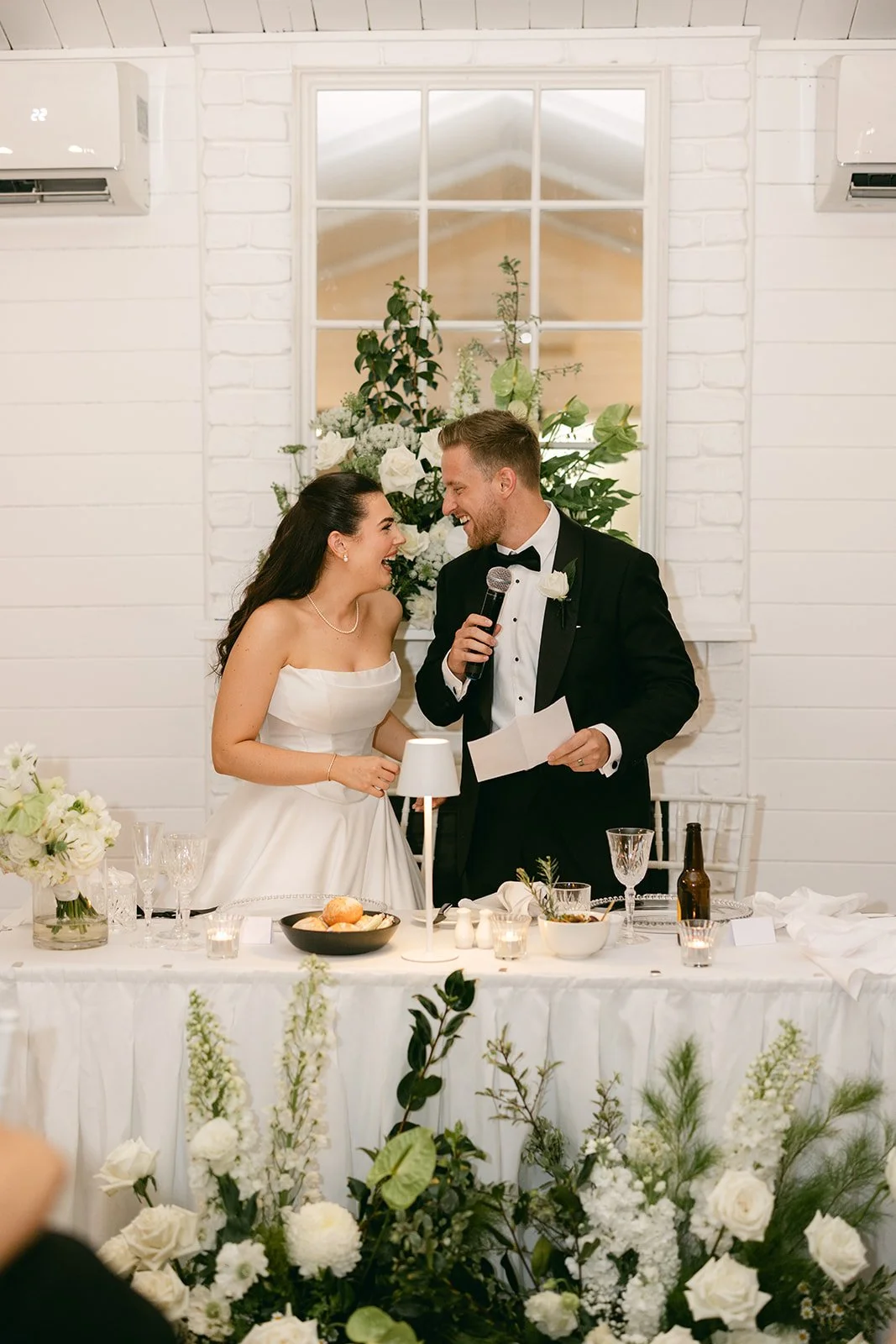 Bride and groom standing behind table smiling at each other.