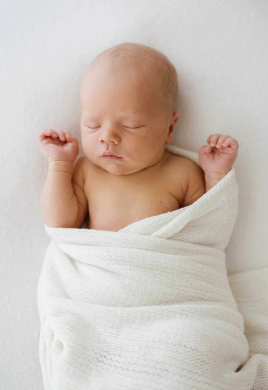 Sleeping newborn wrapped in white cloth, lying on white cushion