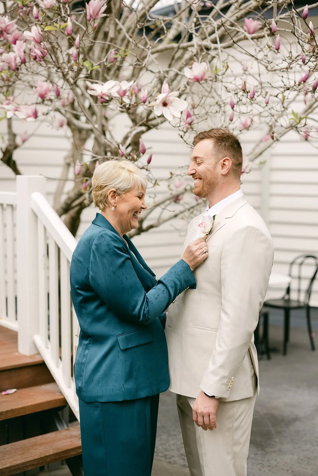 Mother of groom assisting groom getting ready. Both smiling.