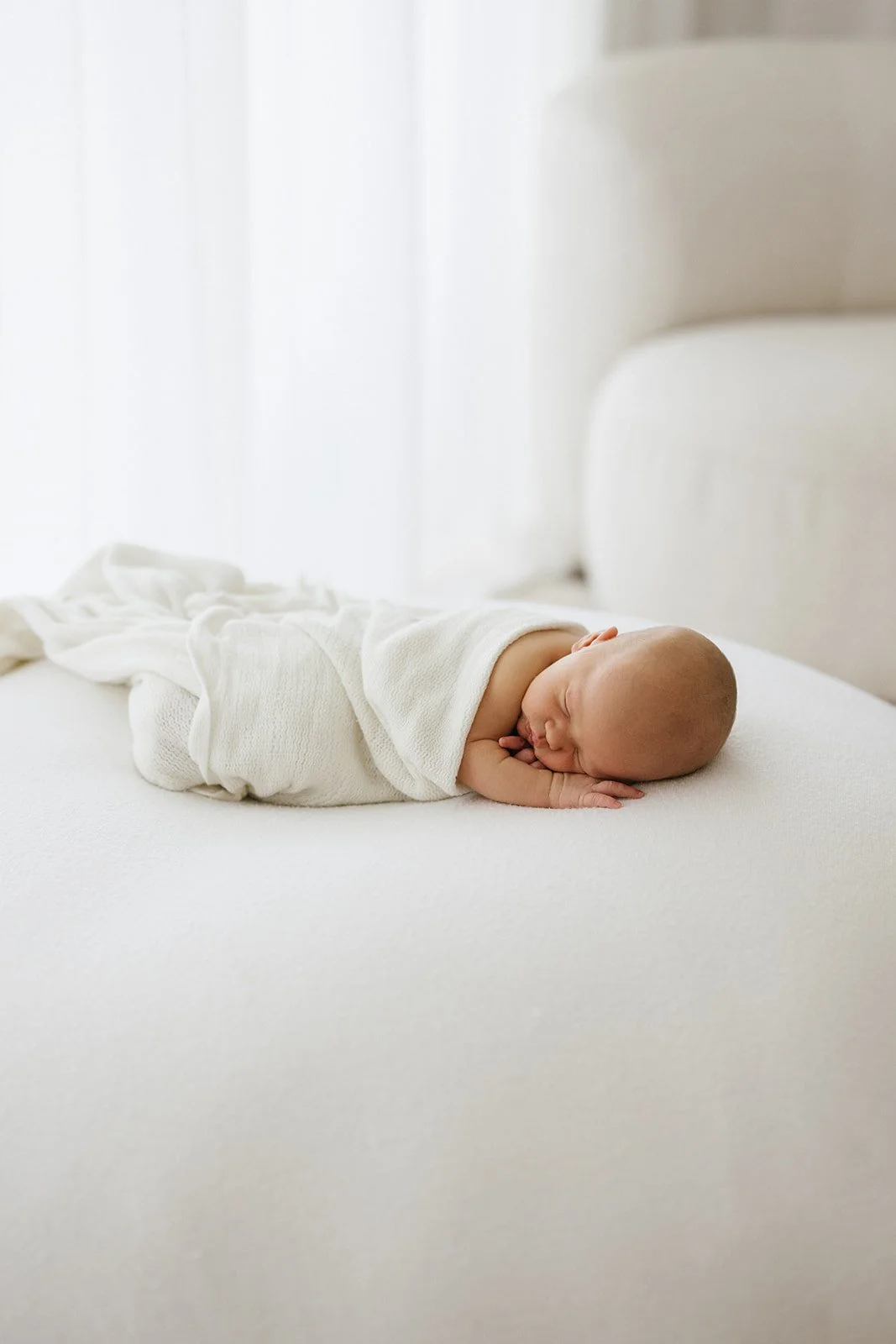 A newborn baby lays on a white newborn photography beanbag on their tummy, the baby is sleeping peacefully with their little hand under their head. The photograph is by Brisbane newborn photography studio Wylde Folk Studio 