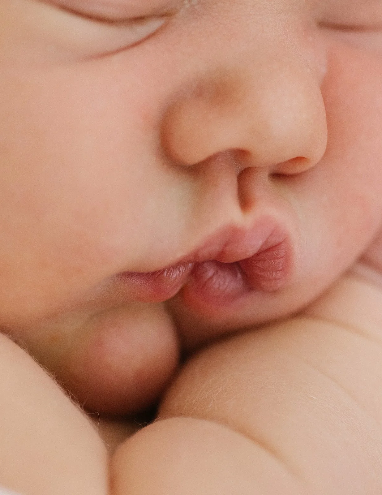 Close-up of a baby's face with closed eyes and lips near another person's skin.
