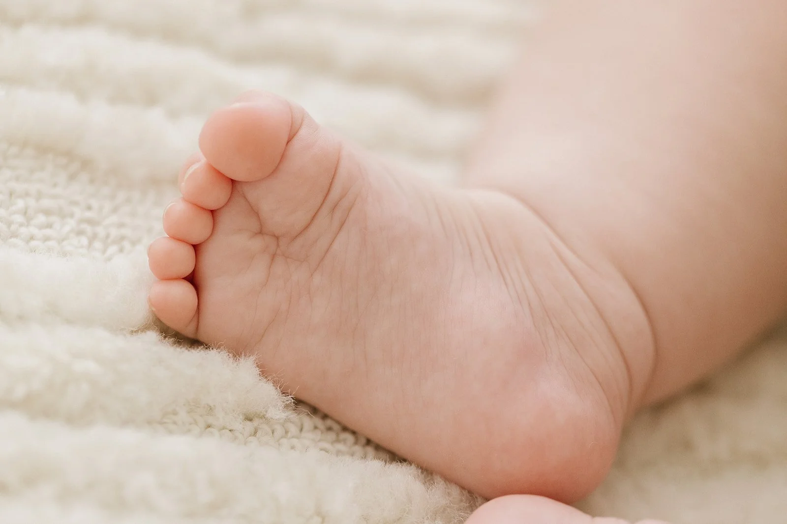 Close-up of a newborn baby's tiny foot resting on a soft, textured fabric.