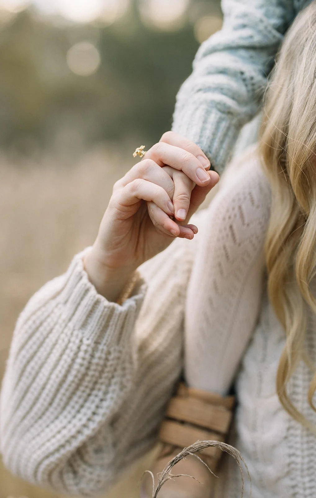 Close-up of a woman holding hands with someone outdoors. The woman is wearing a cream knit sweater, and her long blond hair is visible. Only part of her face is visible. Taken by Wylde Folk Studio, Brisbane. Family photographer.