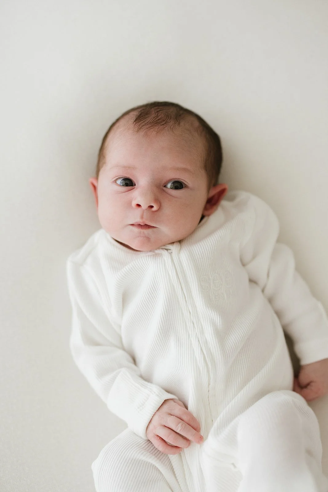 Brisbane newborn photographer Wylde Folk Studio captures an alert newborn baby girl dressed in a white zip up romper