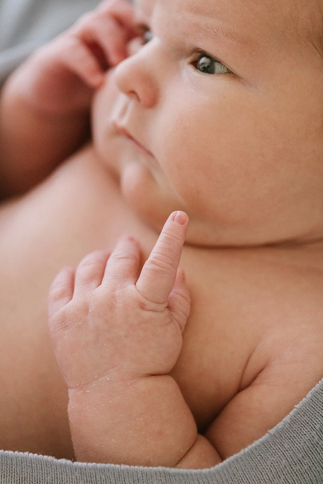 Close-up of an infant with fair skin and blue eyes, holding one finger close to their lips, with another person's hand gently touching the baby's face.