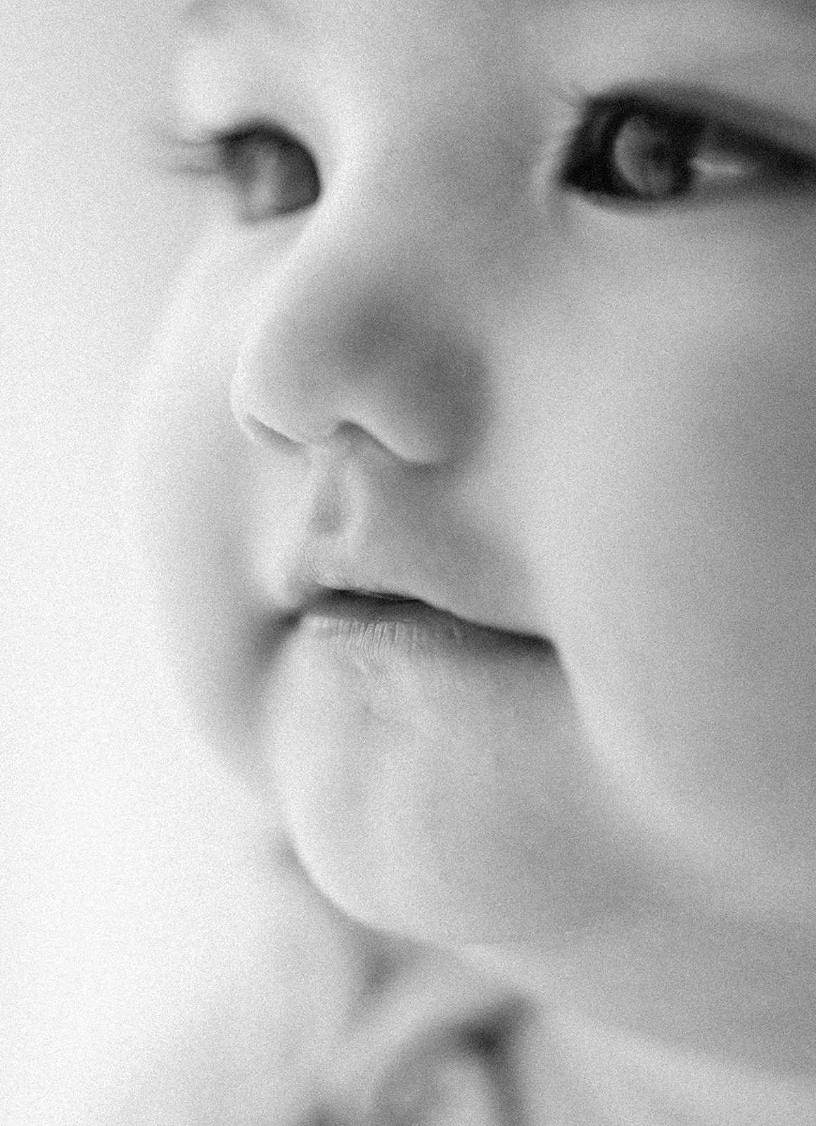 A close-up black and white photograph of a young child's face, focusing on the eyes, nose, and lips, with smooth skin and delicate features. Taken at Wylde Folk Studio - Brisbane photographer.