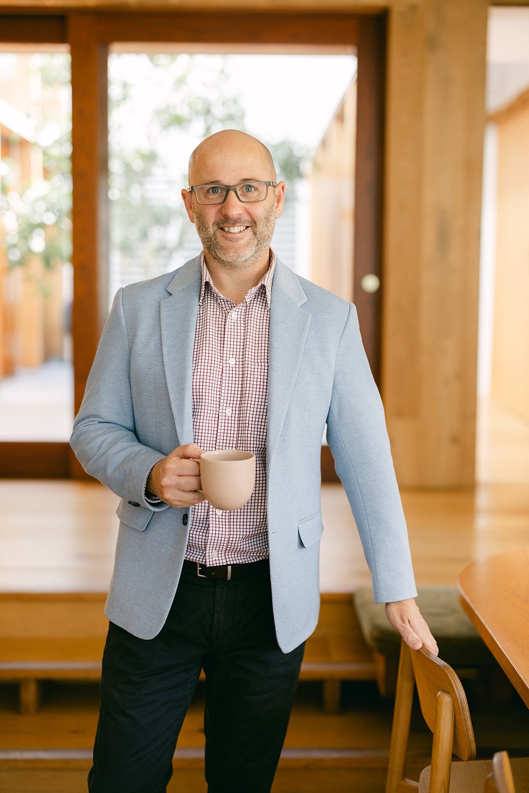 A man in a grey suit stands with a coffee mug for a headshot branding photoshoot