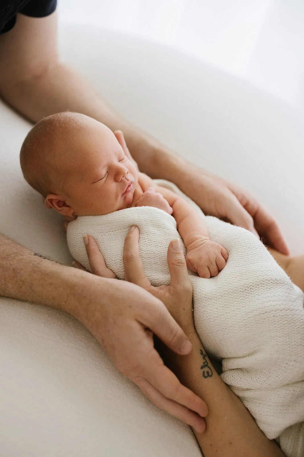 Both mother and father's arms holding sleeping newborn