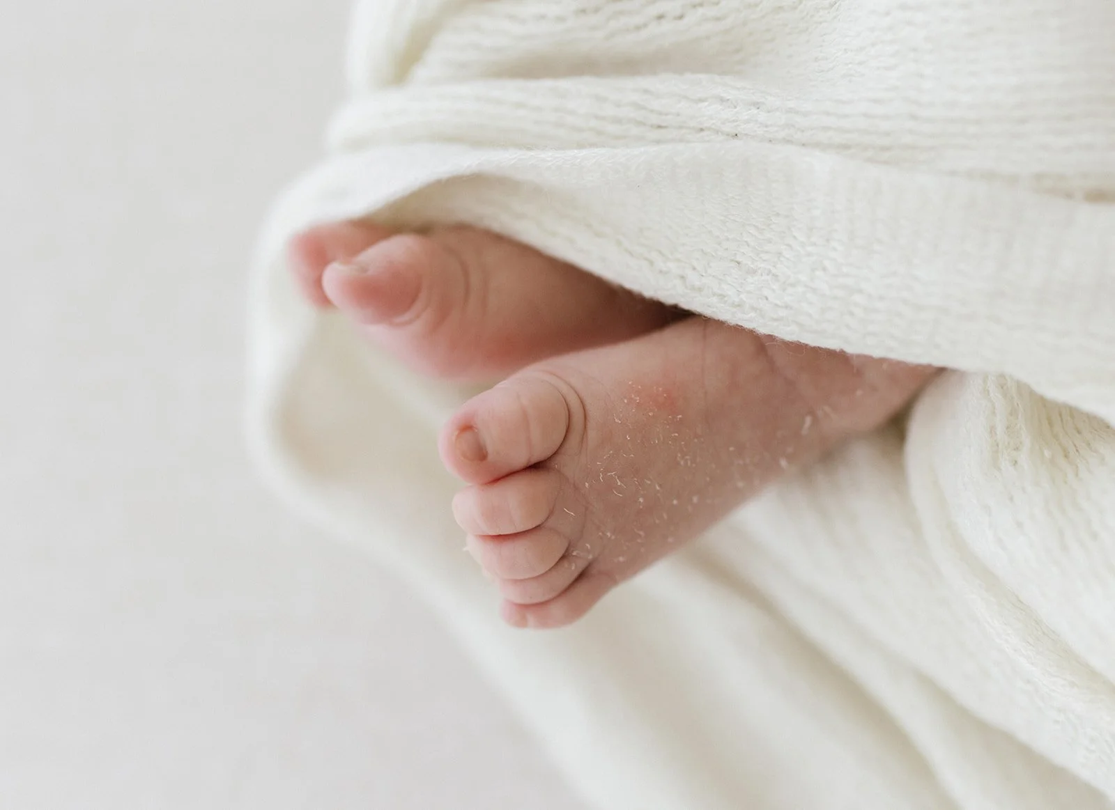 Up-close photo of newborn baby's feet wrapped in white blanket