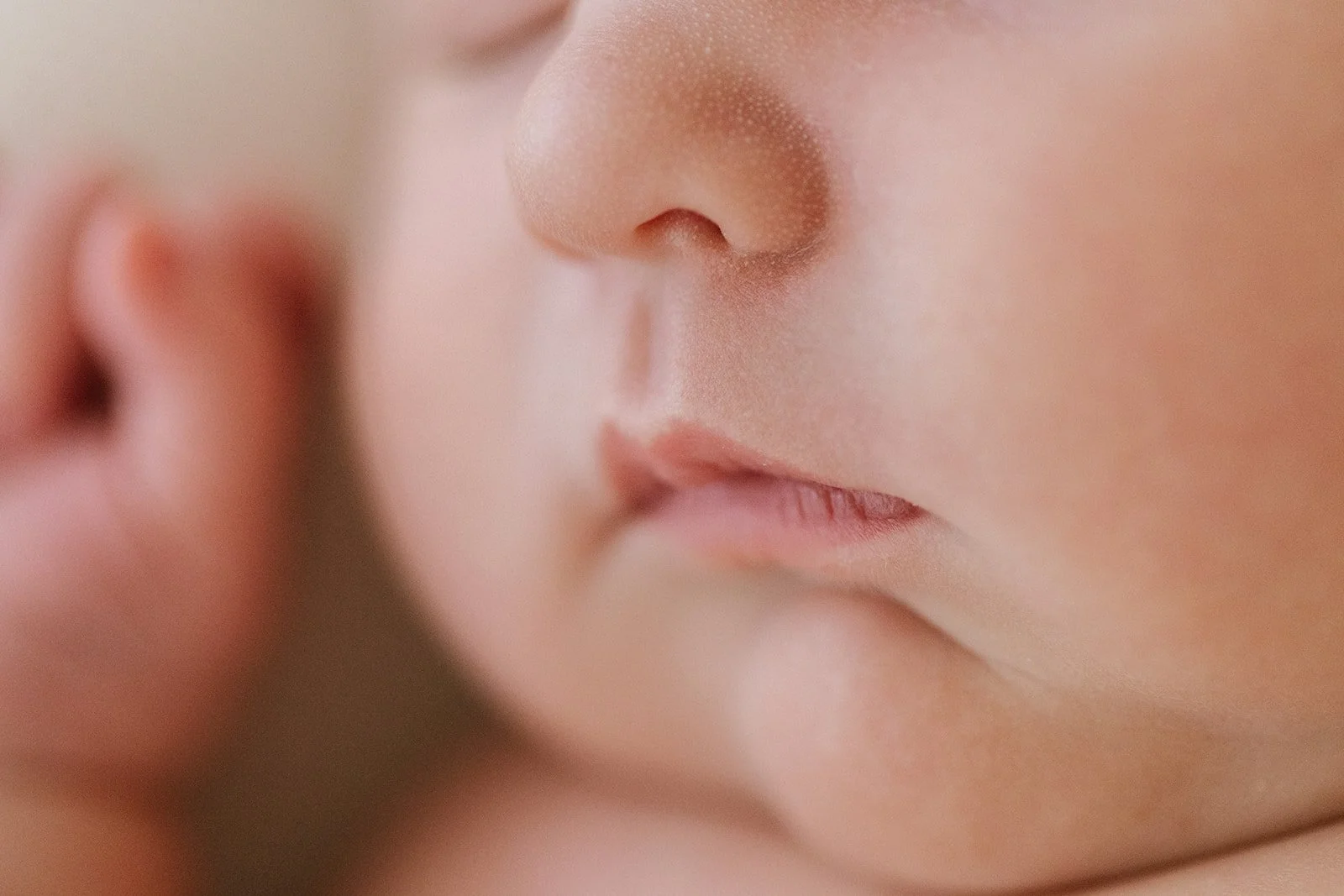 Close-up of a baby's face showing the nose and lips, with another baby's face partially visible in the background.