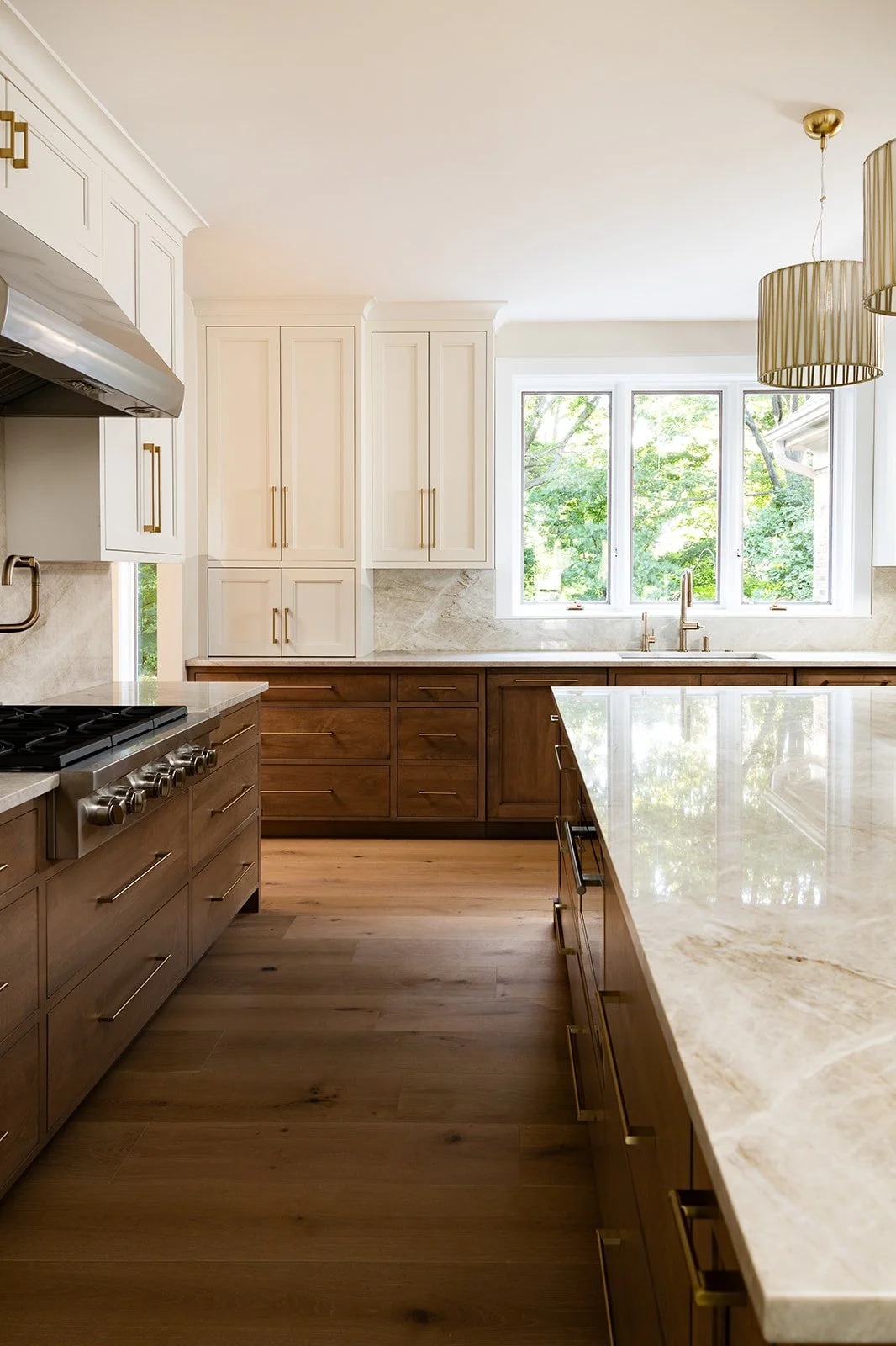 Modern kitchen with wooden cabinets, a light-colored countertop, and a window overlooking green trees.