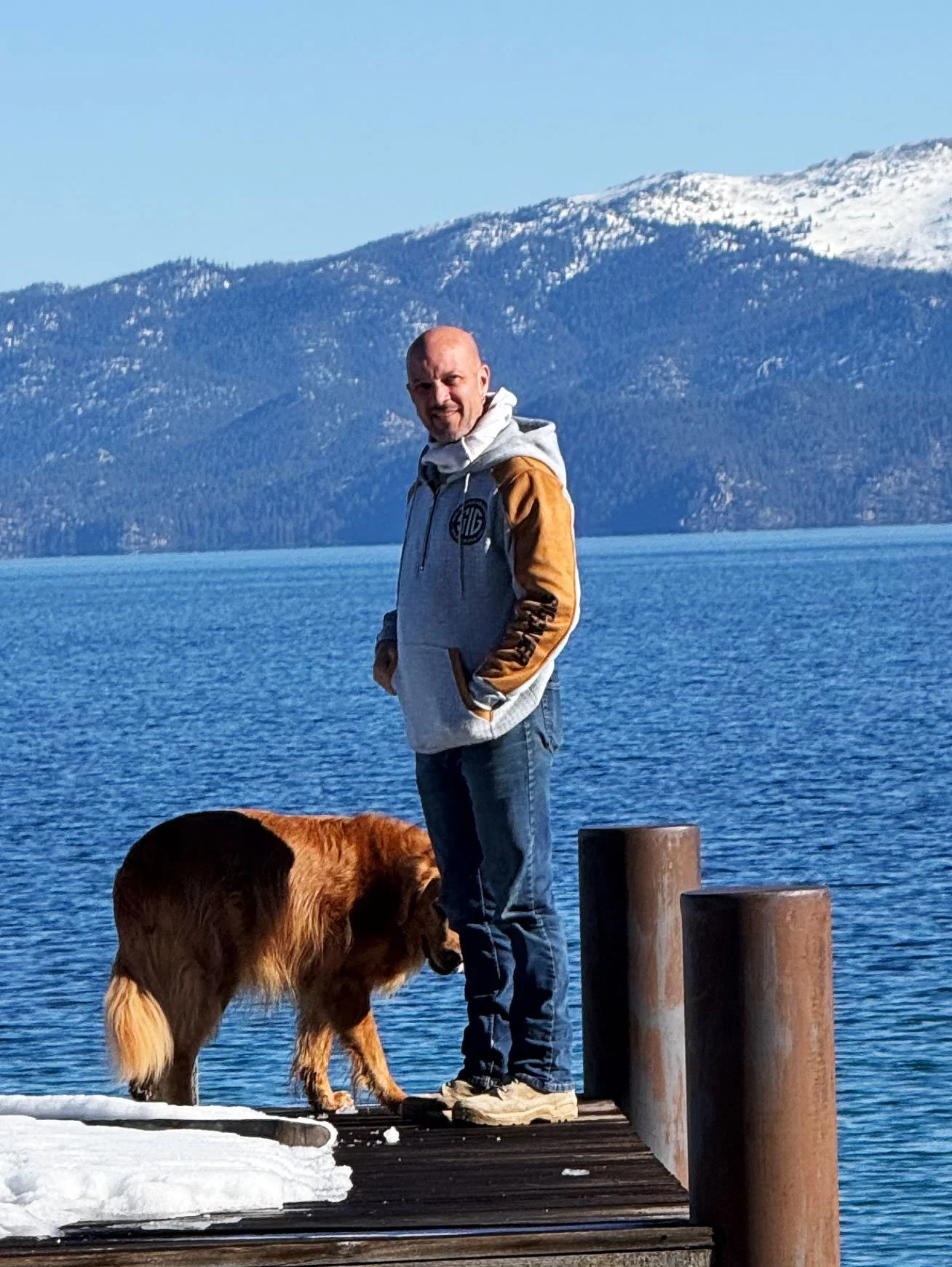 Man standing on a dock on Lake Tahoe with dog and mountains in the background