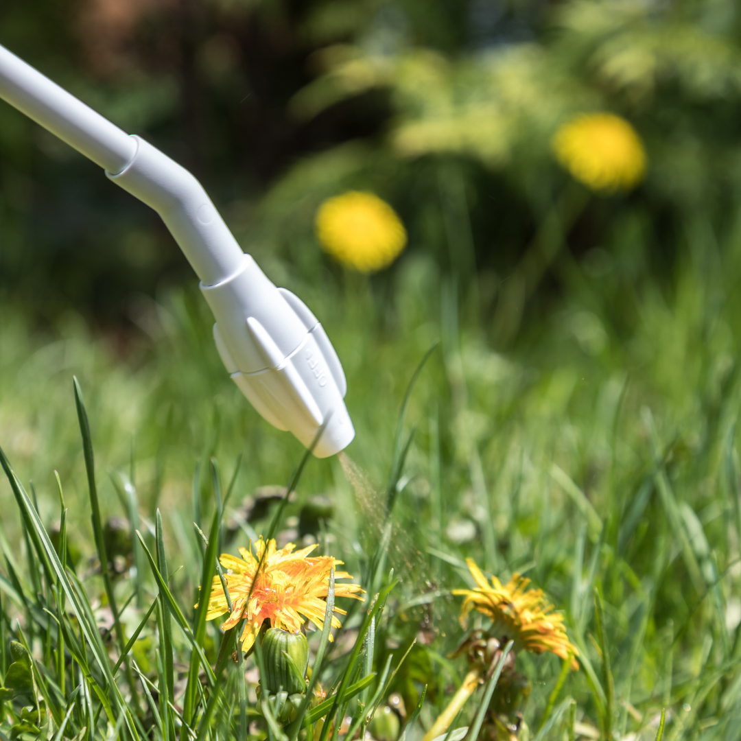 Elevate Your Landscape A bright orange yard sign with black and white text and graphics, warning about herbicide use, placed in green grass, with a stake through it.