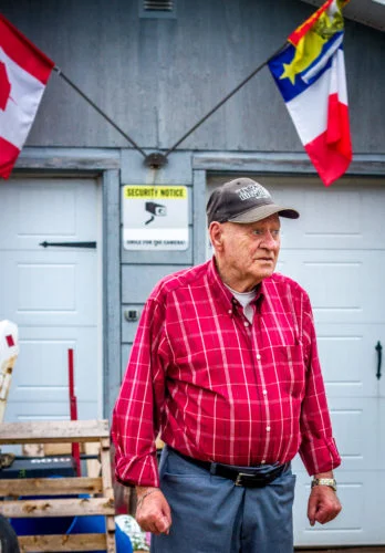 86-year-old Alyre Cormier stands in front of the garage where his son lives on his property in Memramcook, NB. Cormier has lived on the same street his whole life.