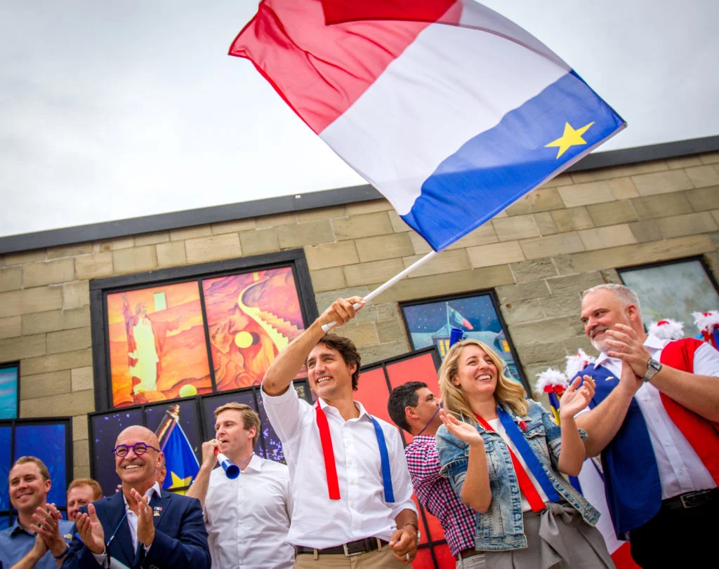Justin Trudeau waves an Acadian flag alongside other dignitaries to begin the 2016 Tintamarre in Caraquet, NB.