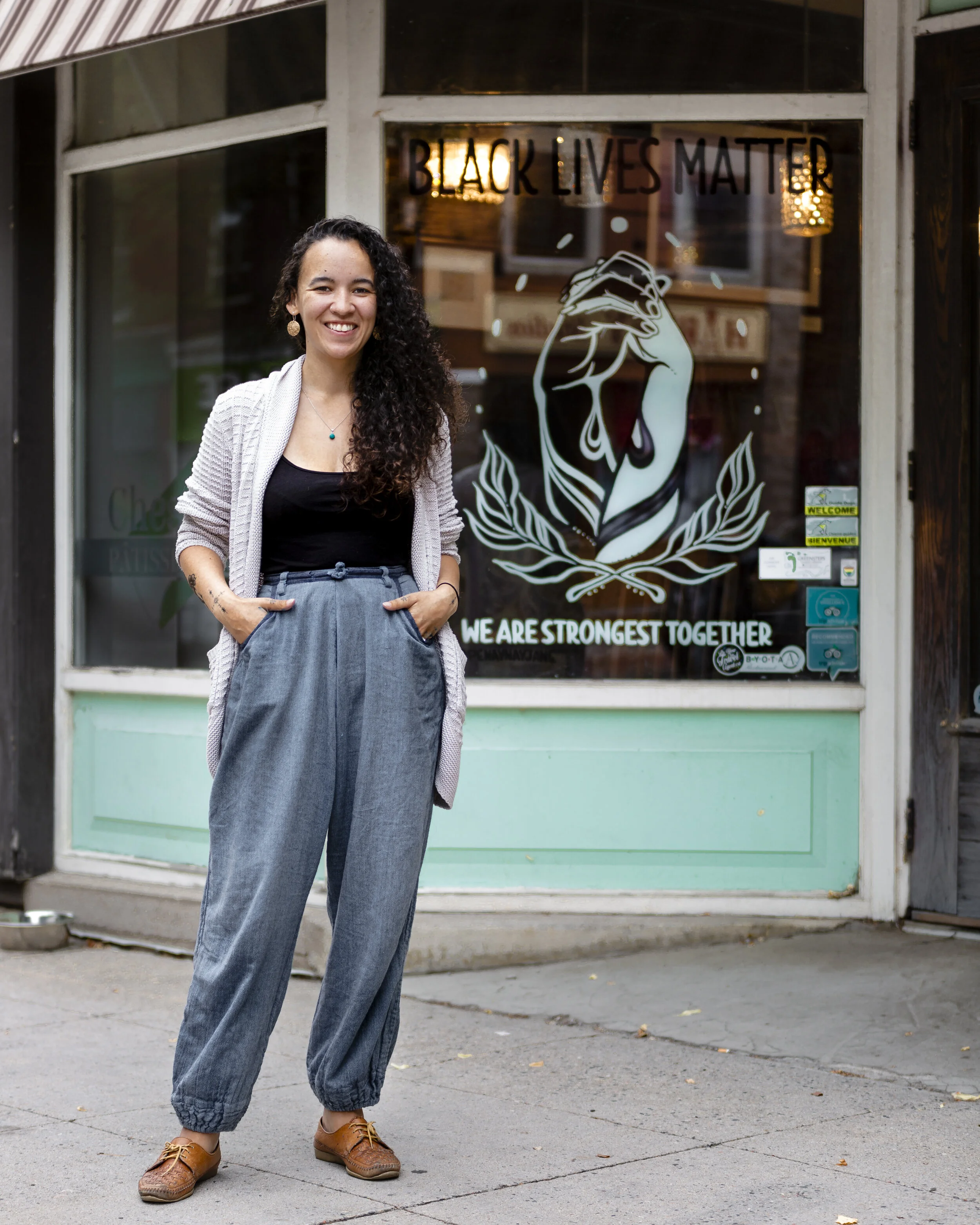 Artist Penny Heather stands in front of her painting on the window of Chess Piece Pâtisserie. Photo by Hailley Fayle.