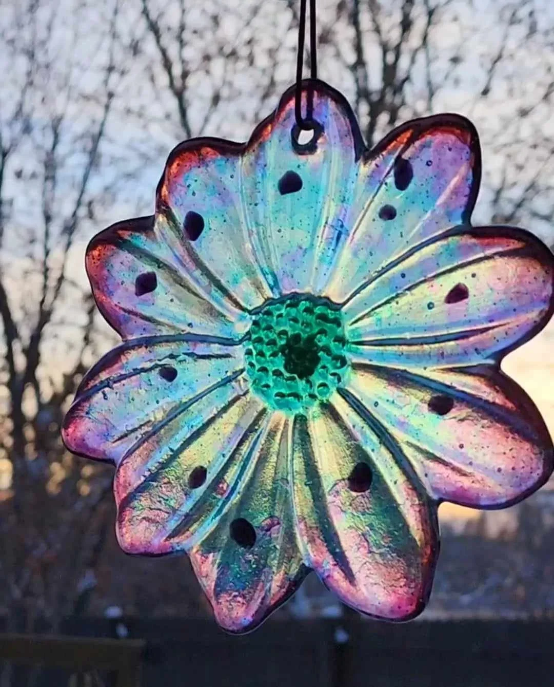 A handcrafted iridescent purple and green glass flower suncatcher memorial hanging outdoors in the Montana sunlight
