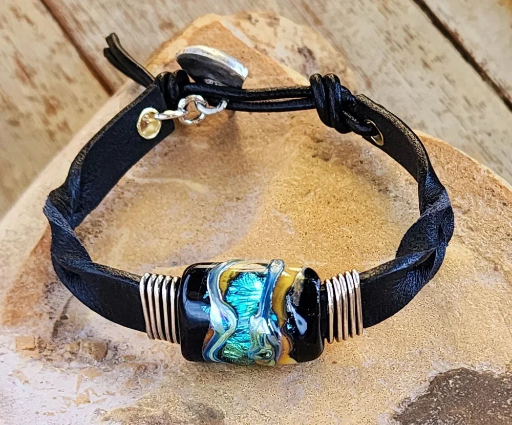 Handcrafted braided black leather memorial bracelet featuring a barrel-shaped Sacred Trace glass infusion with vibrant teal and gold accents, designed as a durable and personal tribute for a cherished loved one