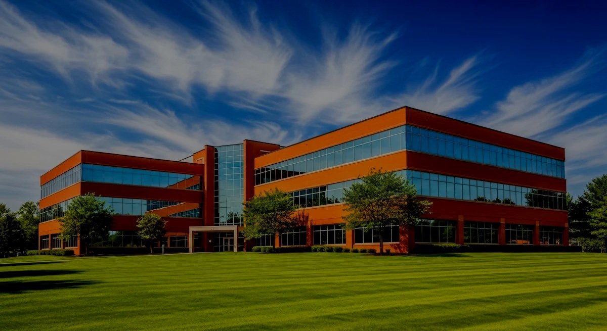 Modern three story corporate office building featuring vibrant orange brick facade large reflective glass windows and meticulously manicured green lawn.jpg