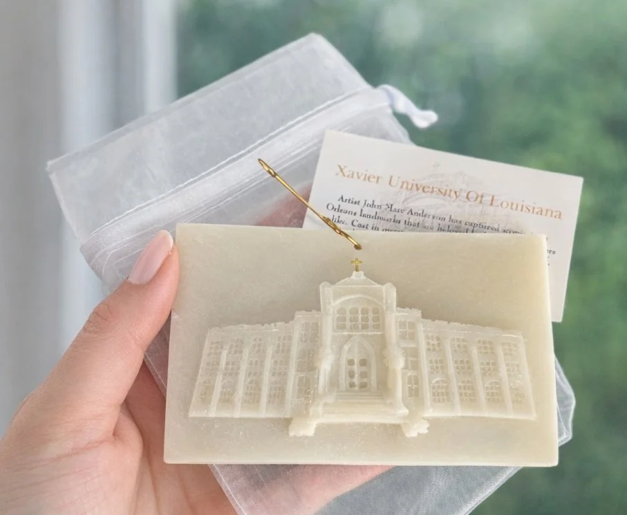 A woman is holding a handcrafted crystal quartz resin memento of Xavier University of Louisiana’s historic administration building, about 3×6 inches, with subtle texture and gold accents, captured against a soft, neutral background.