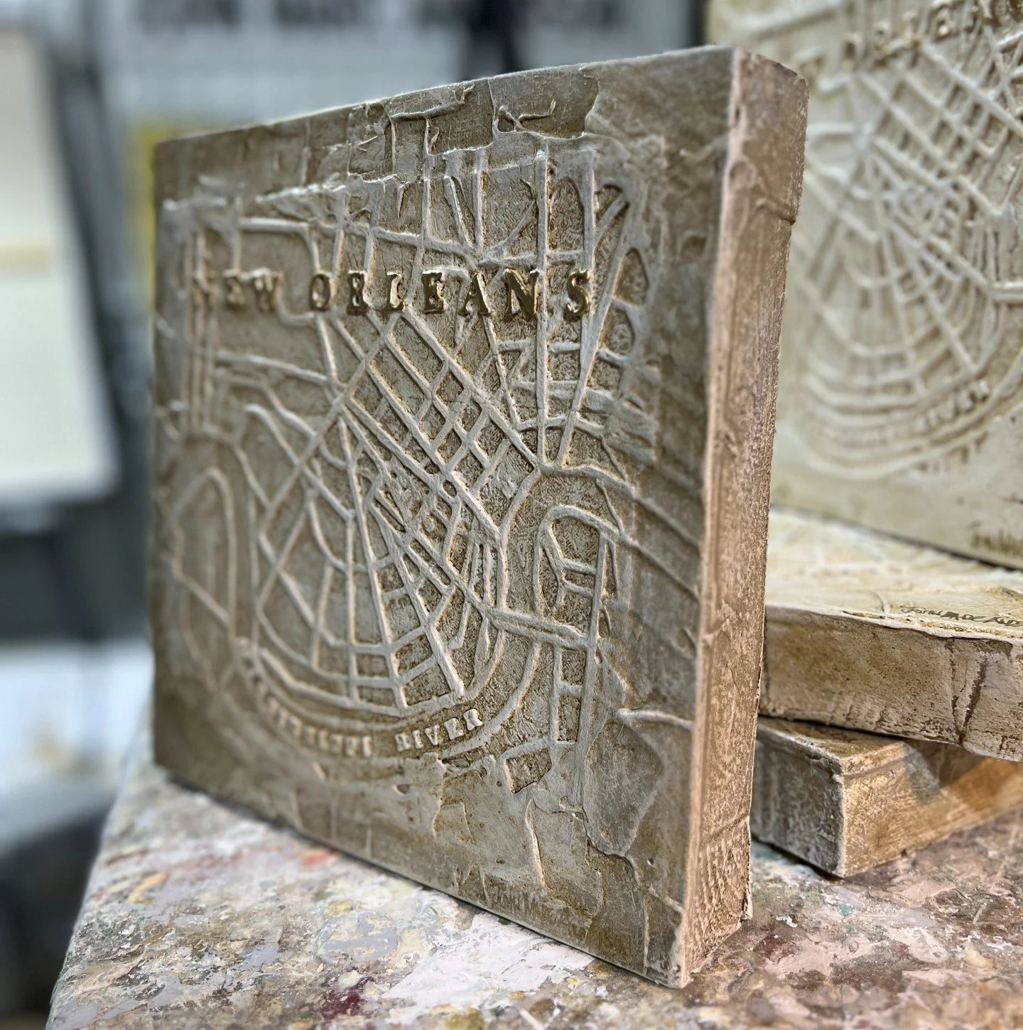 Side view of City Of New Orleans relief map showing raised detail of streets and waterways. Measures 10"x10", signed in gold by John Marc Anderson