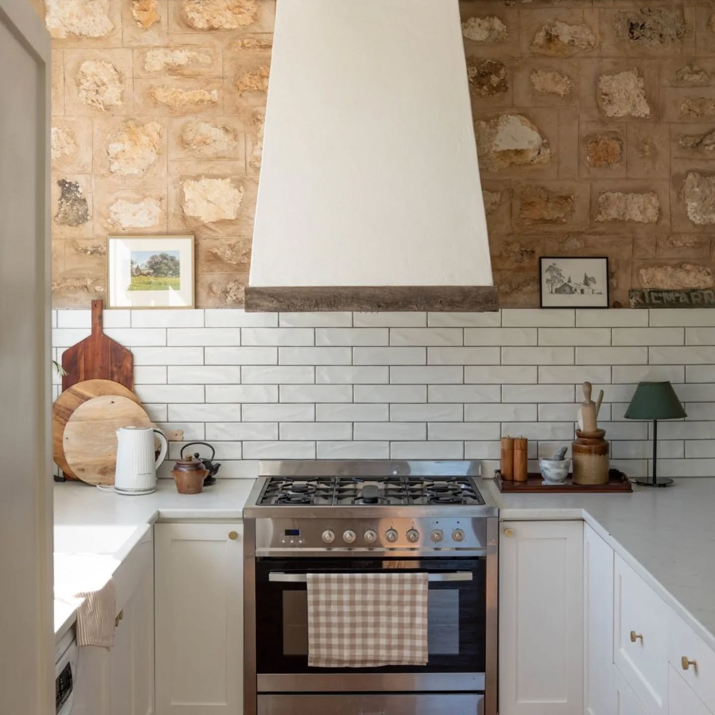 How's this for a country kitchen? ⁠
⁠
There's a lot of balance in this kitchen with the use of classic cabinetry profiling, subway tile and bench top all in neutral tones. ⁠
⁠
This allows for the stone wall, beamed ceiling and custom made range hood 